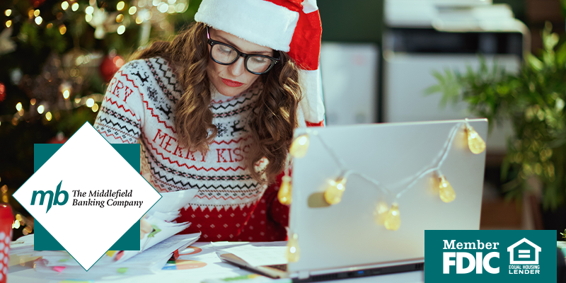 Woman with santa hat and holiday sweater on working at her laptop, looking at business reports