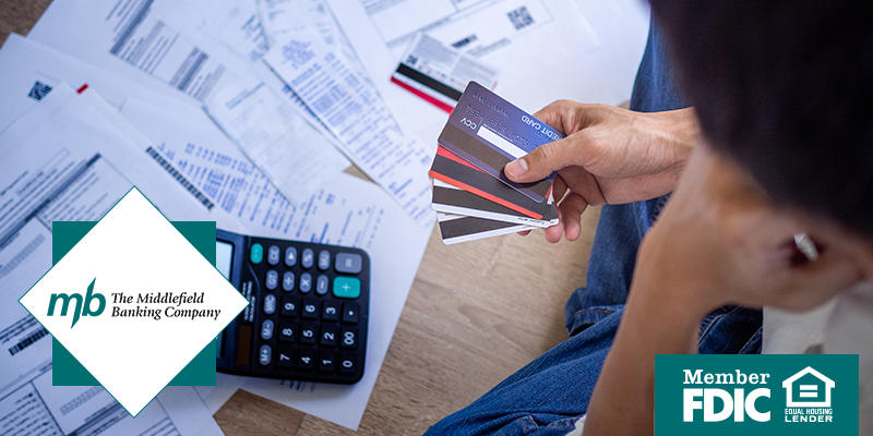 Man holding stack of credit cards in his hands with a calculator on the floor and various financial reports spread about the floor