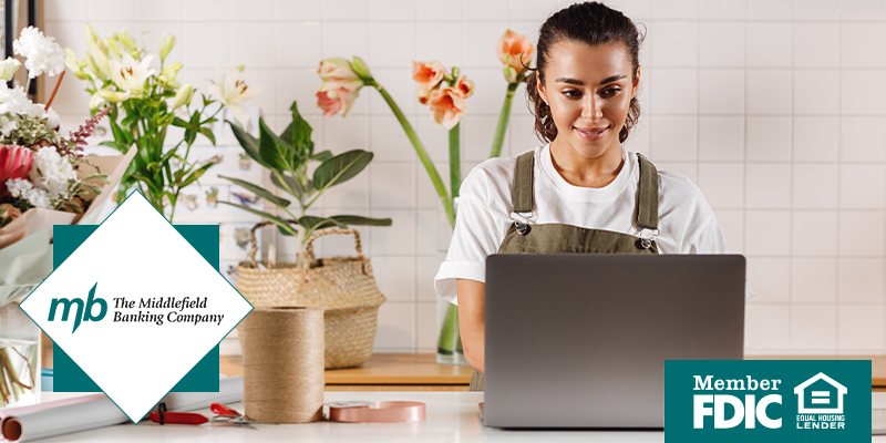 Woman smiling at her laptop wearing an apron and working at a local flower shop