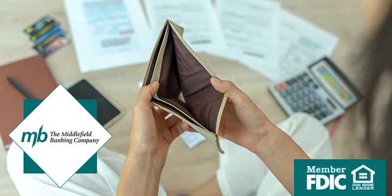 Young person holding open an empty wallet with budgeting materials in the background